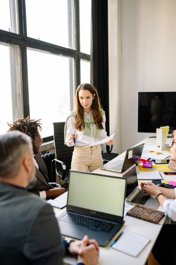 Group of colleagues collaborating in a modern office meeting room, discussing ideas with laptops and paperwork.