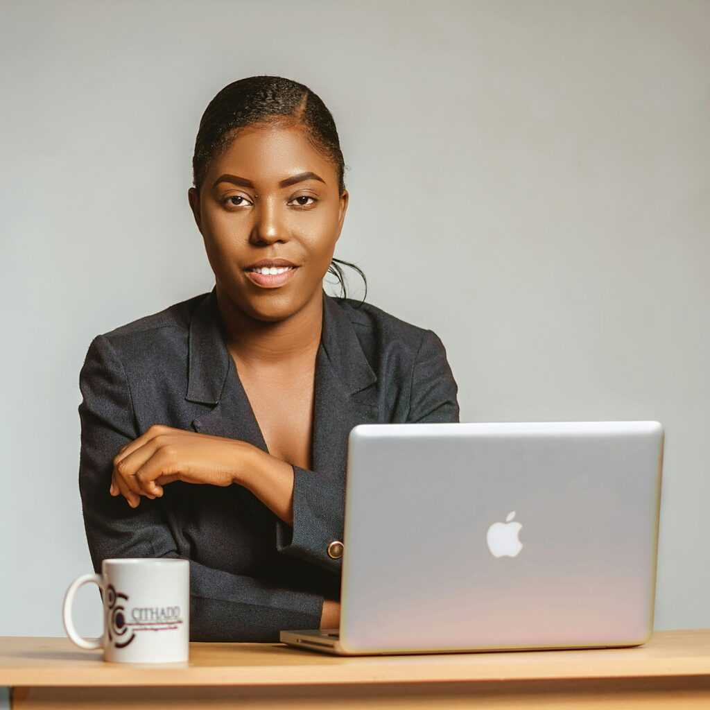 Confident black woman in blazer using laptop at wooden desk.