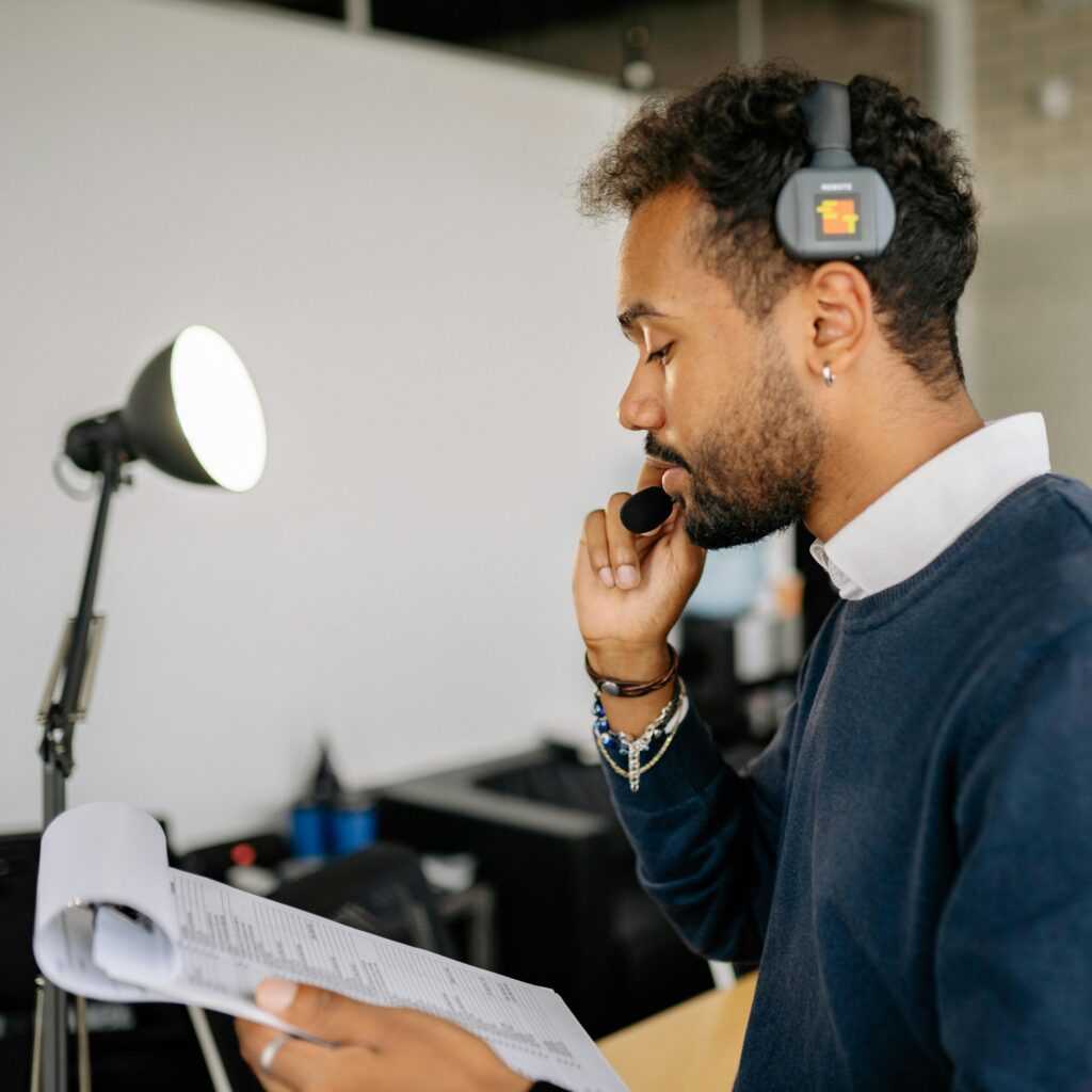 Young man in studio reading script with headphones, focused on task at hand.