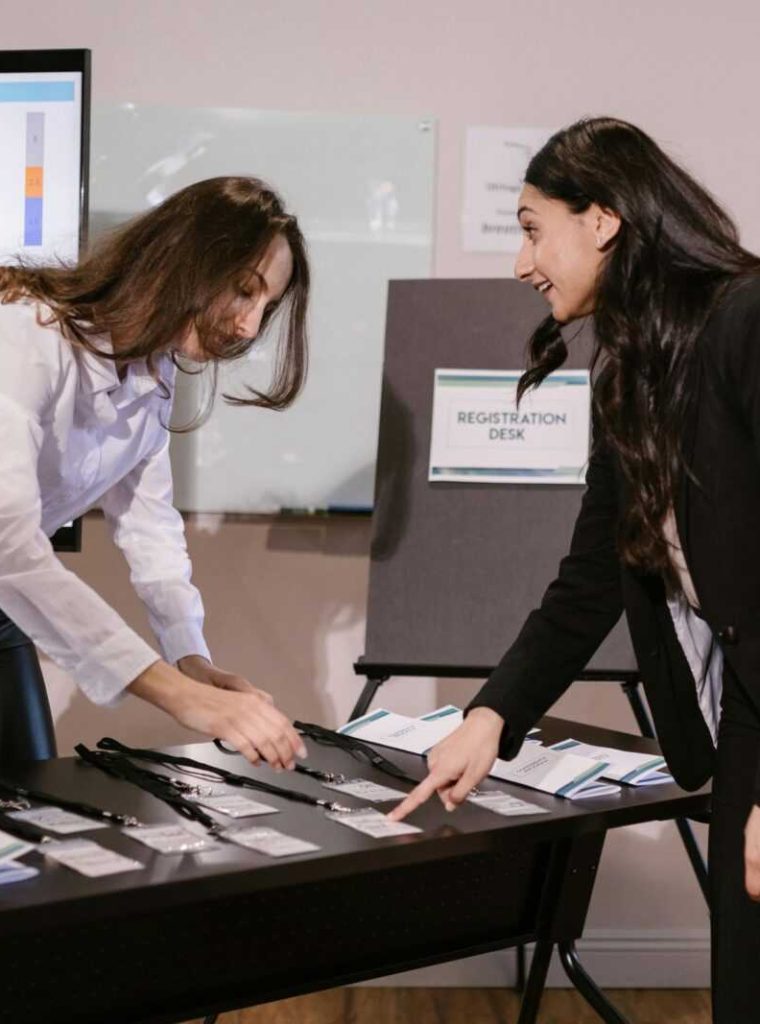 Two women arranging name badges at a registration desk during a corporate event.